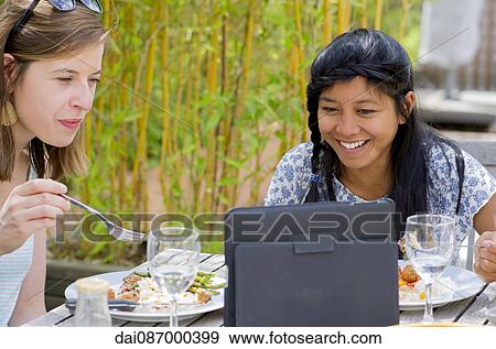 Women watching digital tablet while eating outdoors View Large Photo Image Stock Photo - Women watching digital tablet while eating outdoors. Fotosearch