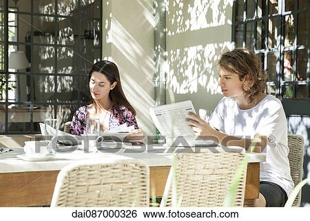Young couple reading newspaper while enjoying breakfast in backyard View Large Photo Image Stock Photograph - Young couple reading newspaper while enjoying breakfast in backyard. Fotosearch
