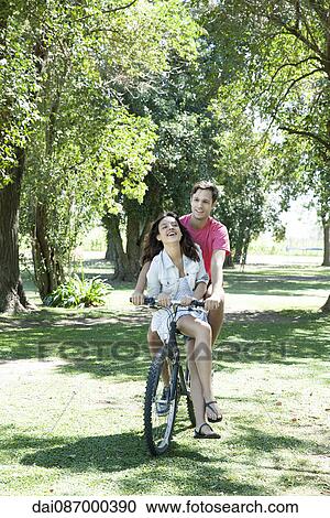 Young couple riding bicycle together with girlfriend seated sidesaddle on crossbar View Large Photo Image Stock Image - Young couple riding bicycle together with girlfriend seated sidesaddle on crossbar. Fotosearch