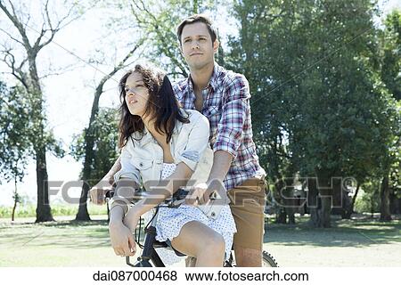 Young couple riding bicycle together with girlfriend seated sidesaddle on crossbar View Large Photo Image Stock Photo - Young couple riding bicycle together with girlfriend seated sidesaddle on crossbar. Fotosearch