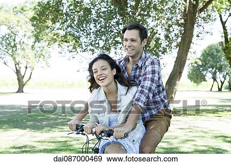 Young couple riding bicycle together with girlfriend seated sidesaddle on crossbar View Large Photo Image Stock Photo - Young couple riding bicycle together with girlfriend seated sidesaddle on crossbar. Fotosearch