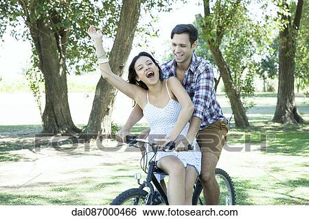 Young couple riding bicycle together with girlfriend seated sidesaddle on crossbar View Large Photo Image Stock Photograph - Young couple riding bicycle together with girlfriend seated sidesaddle on crossbar. Fotosearch