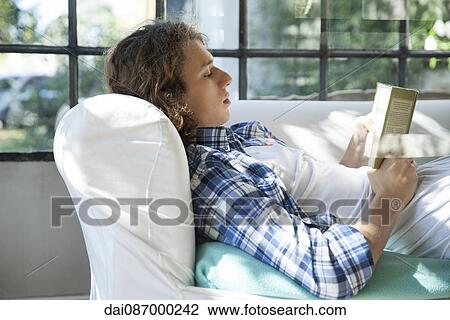 Young man reading book on couch View Large Photo Image Stock Image - Young man reading book on couch. Fotosearch
