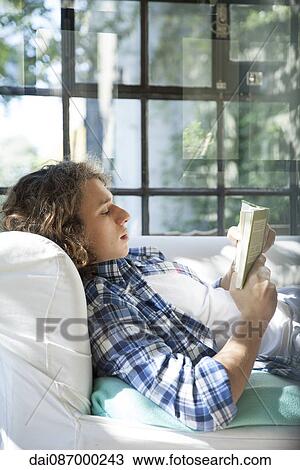 Young man reading book on couch View Large Photo Image Stock Image - Young man reading book on couch. Fotosearch