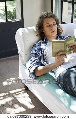Young man reading book on couch View Large Photo Image Stock Photo - Young man reading book on couch. Fotosearch