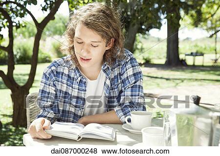 Stock Photo - Young man reading book while enjoying cup of coffee. Fotosearch