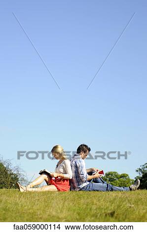 Picture - Couple sitting back to back reading in park. Fotosearch
