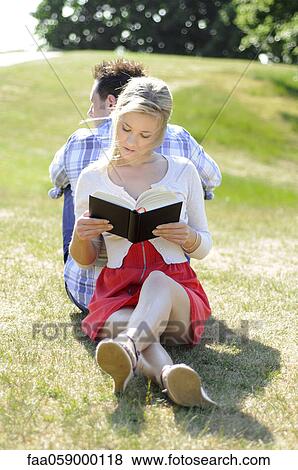 Couple sitting back to back reading in park View Large Photo Image Stock Photo - Couple sitting back to back reading in park. Fotosearch