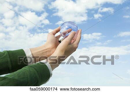 Person holding light bulb in cupped hands View Large Photo Image Picture - Person holding light bulb in cupped hands. Fotosearch