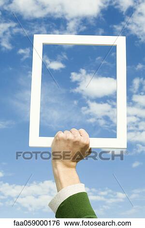 Stock Photograph - Person holding picture frame in front of sky. Fotosearch