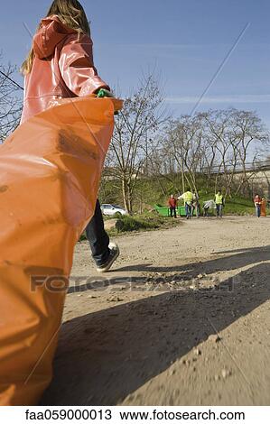 Stock Image - Picking up roadside litter, dragging full garbage bag. Fotosearch