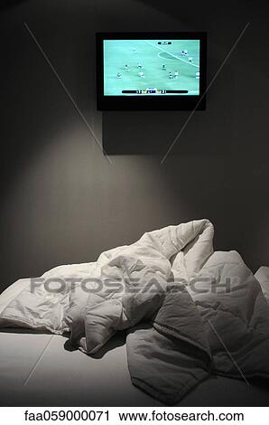 Stock Image - Sports match on flat screen TV mounted over bed. Fotosearch