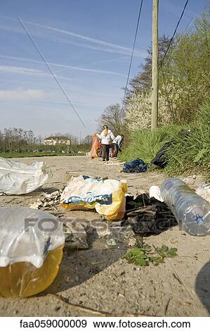 Stock Photo - Trash dumped on dirt road, volunteers in background cleaning up. Fotosearch