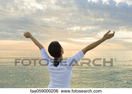 Woman watching sunset at the beach, arms raised in the air View Large Photo Image Stock Photograph - Woman watching sunset at the beach, arms raised in the air. Fotosearch