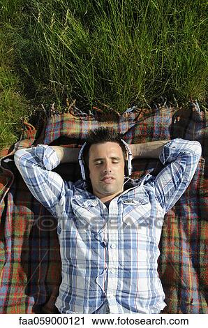 Young man lying on blanket and listening to headphones outdoors View Large Photo Image Stock Image - Young man lying on blanket and listening to headphones outdoors. Fotosearch