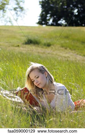 Stock Photo - Young woman lying on ground reading book. Fotosearch