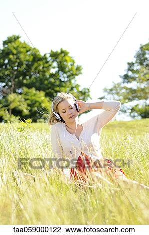 Young woman sitting in tall grass listening to headphones View Large Photo Image Stock Image - Young woman sitting in tall grass listening to headphones. Fotosearch