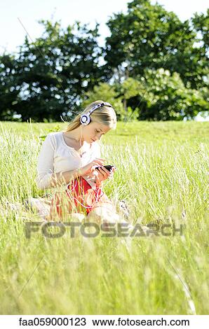 Young woman sitting in tall grass listening to headphones View Large Photo Image Stock Image - Young woman sitting in tall grass listening to headphones. Fotosearch