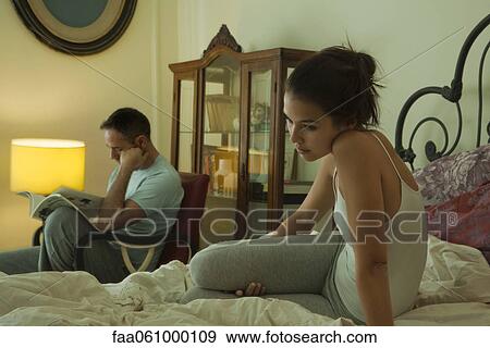 Wife sitting on bed alone in thought, husband reading in background View Large Photo Image Stock Photo - Wife sitting on bed alone in thought, husband reading in background. Fotosearch
