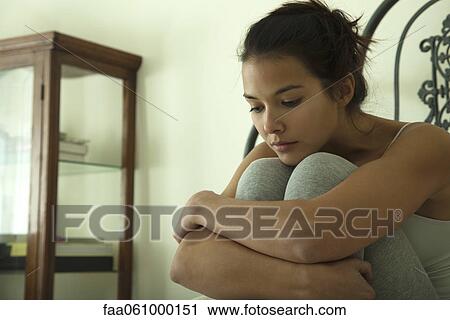 Young woman hugging knees, looking down in thought, portrait View Large Photo Image Stock Image - Young woman hugging knees, looking down in thought, portrait. Fotosearch