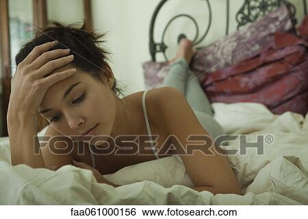 Stock Photograph - Young woman lying on bed, portrait. Fotosearch