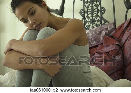 Young woman sitting on bed, looking down in thought, portrait View Large Photo Image Stock Image - Young woman sitting on bed, looking down in thought, portrait. Fotosearch