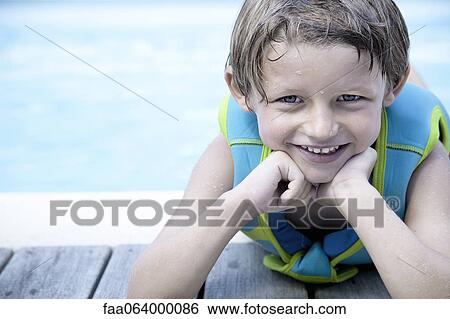Stock Photograph - Boy in life jacket leaning against side of pool, portrait. Fotosearch