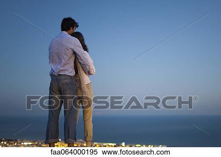 Couple standing on edge of infinity pool at dusk, looking at sea View Large Photo Image Stock Photography - Couple standing on edge of infinity pool at dusk, looking at sea. Fotosearch