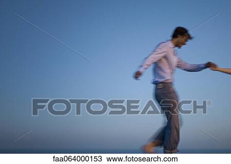 Stock Image - Couple walking together along edge of infinity pool, holding hands. Fotosearch