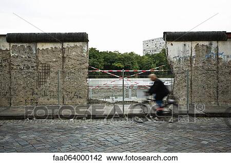 Stock Image - Germany, Berlin, person bicycling past dismantled section of the Berlin Wall. Fotosearch