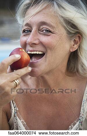 Picture - Mature woman biting into apple. Fotosearch