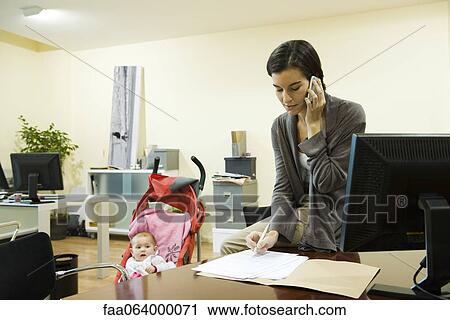 Stock Image - Woman working in office with baby in stroller nearby. Fotosearch