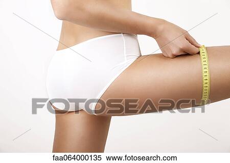 Stock Photography - Young woman measuring thigh with measuring tape, cropped. Fotosearch