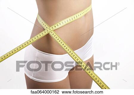 Stock Image - Young woman measuring waist with measuring tape, cropped. Fotosearch