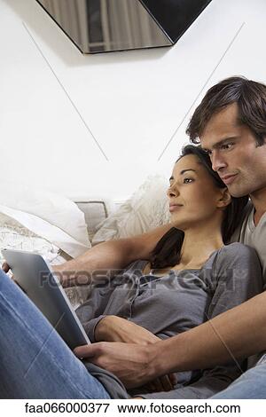 Couple relaxing together, man looking at digital tablet View Large Photo Image Stock Photo - Couple relaxing together, man looking at digital tablet. Fotosearch