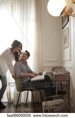 Couple talking while looking at magazine together View Large Photo Image Stock Photography - Couple talking while looking at magazine together. Fotosearch
