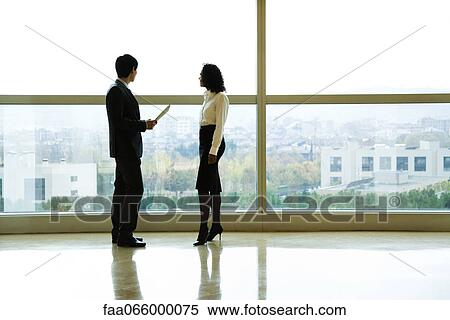 Executives standing by window talking View Large Photo Image Stock Photography - Executives standing by window talking. Fotosearch
