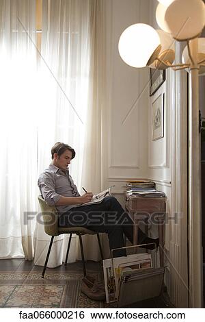 Man sitting at desk reading magazine View Large Photo Image Stock Photograph - Man sitting at desk reading magazine. Fotosearch