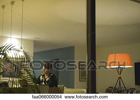 Man using laptop in living room, viewed through window View Large Photo Image Picture - Man using laptop in living room, viewed through window. Fotosearch