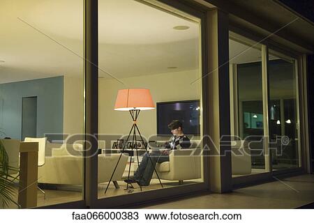 Man using laptop in living room, viewed through window View Large Photo Image Stock Image - Man using laptop in living room, viewed through window. Fotosearch