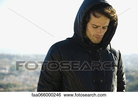 Man wearing hooded jacket, looking down, portrait View Large Photo Image Stock Photograph - Man wearing hooded jacket, looking down, portrait. Fotosearch