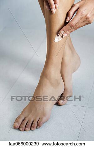 Stock Photo - Woman applying moisturizer to legs, cropped. Fotosearch