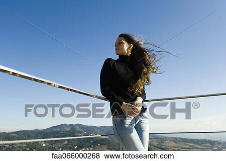 Stock Photo - Woman leaning against railing, looking at view. Fotosearch