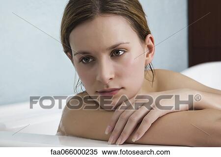 Stock Photography - Woman relaxing in bathtub, looking away in thought. Fotosearch
