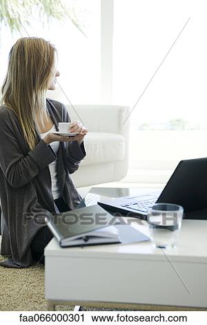 Woman relaxing in living room with cup of coffee and laptop, gazing out window View Large Photo Image Stock Image - Woman relaxing in living room with cup of coffee and laptop, gazing out window. Fotosearch