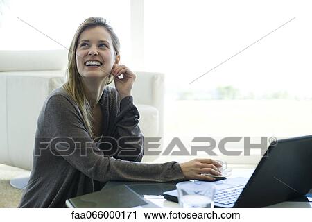 Woman sitting at coffee table with laptop computer and coffee, looking up and smiling View Large Photo Image Stock Image - Woman sitting at coffee table with laptop computer and coffee, looking up and smiling. Fotosearch