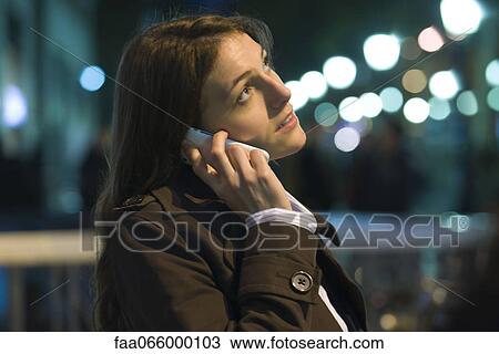 Stock Image - Woman talking on cell phone at night, looking upset. Fotosearch