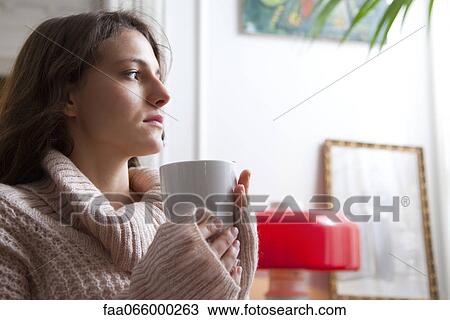 Young woman holding coffee cup, looking away in thought View Large Photo Image Stock Image - Young woman holding coffee cup, looking away in thought. Fotosearch