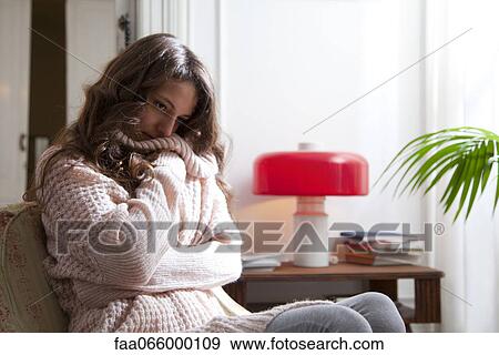 Young woman wearing sweater sitting with arms folded, looking down in thought View Large Photo Image Stock Photo - Young woman wearing sweater sitting with arms folded, looking down in thought. Fotosearch