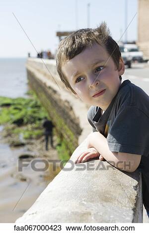 Stock Image - Boy leaning against waterfront railing, looking at view. Fotosearch